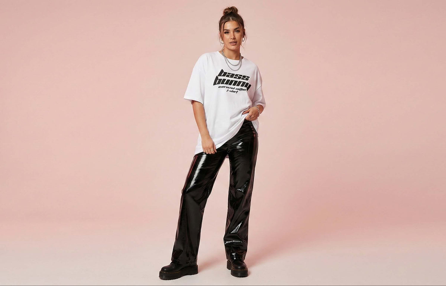 Person wearing a white t-shirt with text and black pants on a pink background